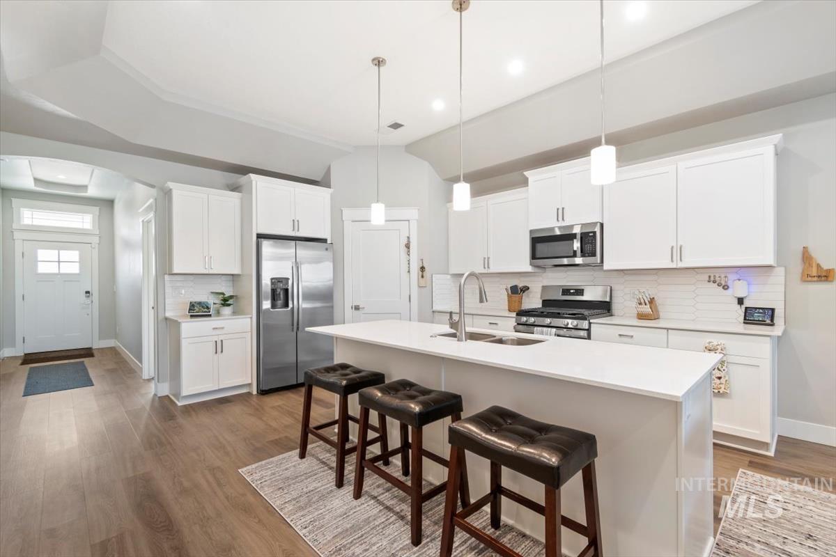 Kitchen featuring decorative backsplash, stainless steel appliances, a kitchen bar, decorative light fixtures, and white cabinetry