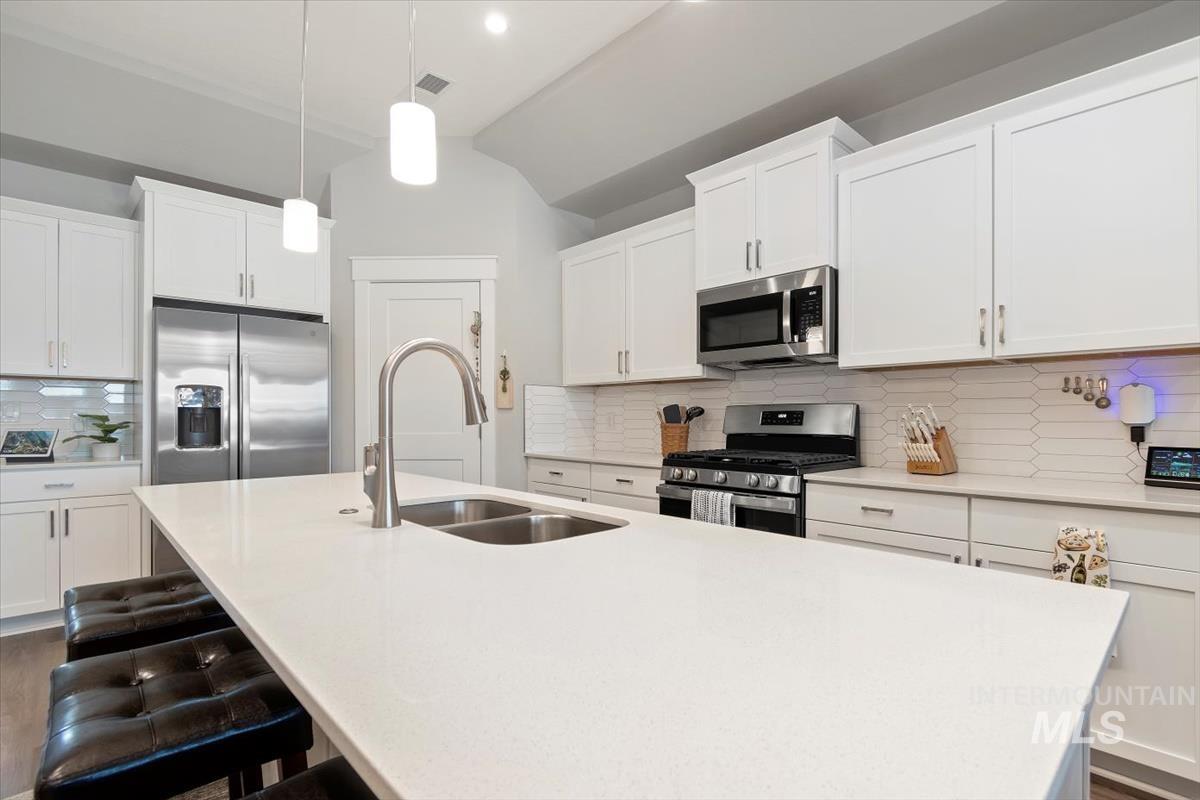 Kitchen with tasteful backsplash, appliances with stainless steel finishes, white cabinetry, an island with sink, and lofted ceiling