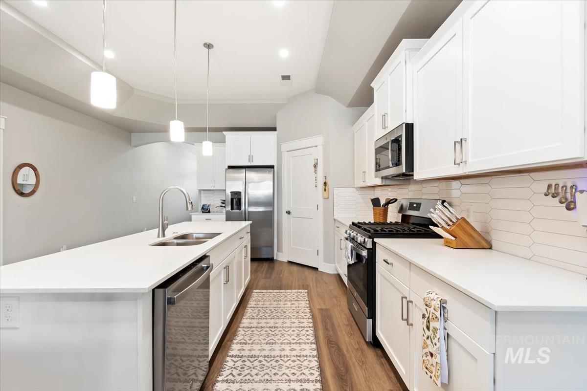 Kitchen with appliances with stainless steel finishes, dark wood-type flooring, backsplash, decorative light fixtures, and a center island with sink