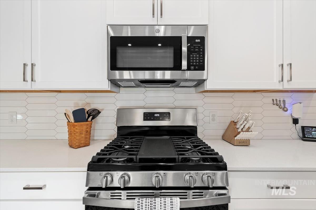 Kitchen featuring stainless steel appliances, white cabinets, tasteful backsplash, and light stone countertops