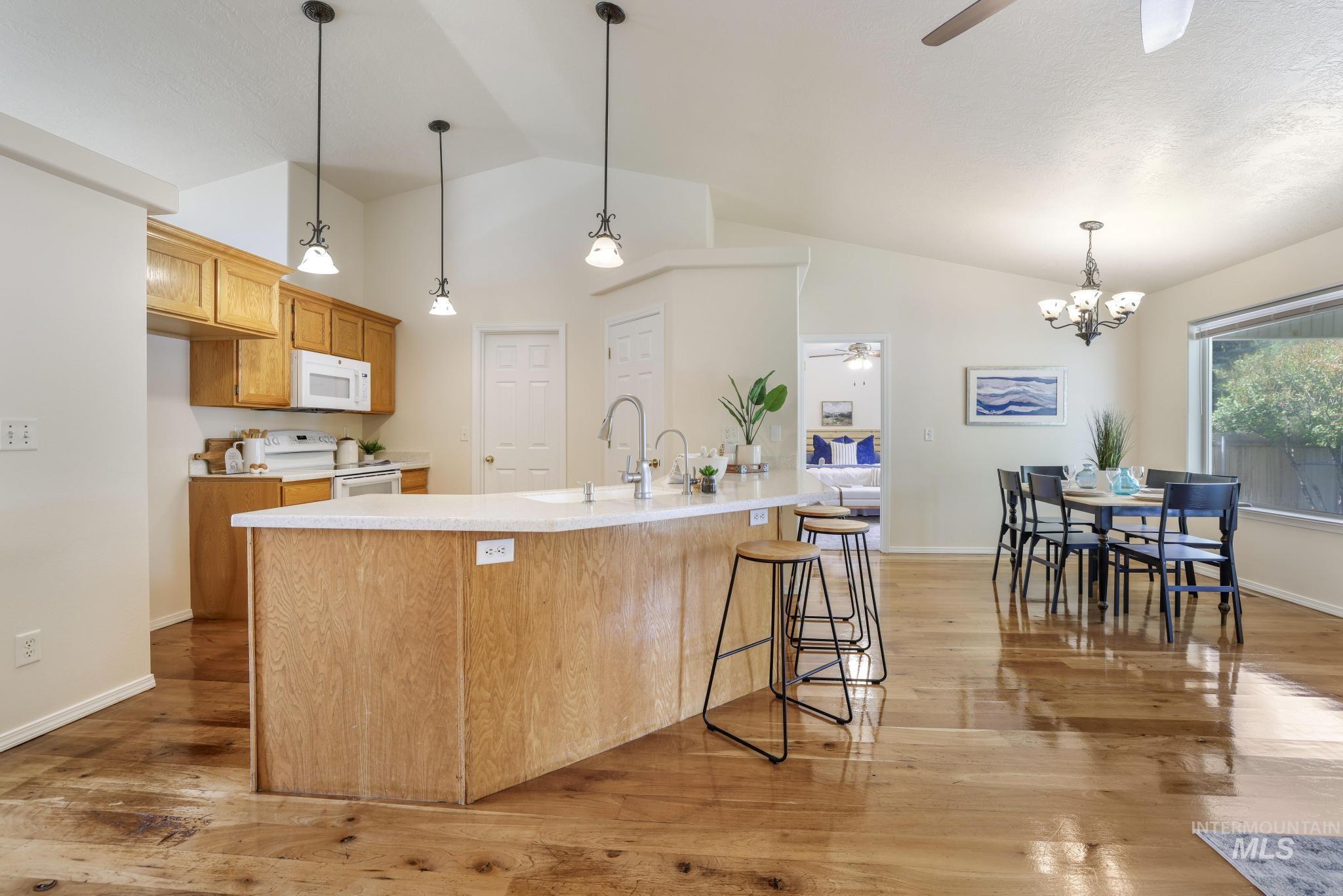 Kitchen with ceiling fan, light wood-style flooring, lofted ceiling, hanging light fixtures, and white appliances