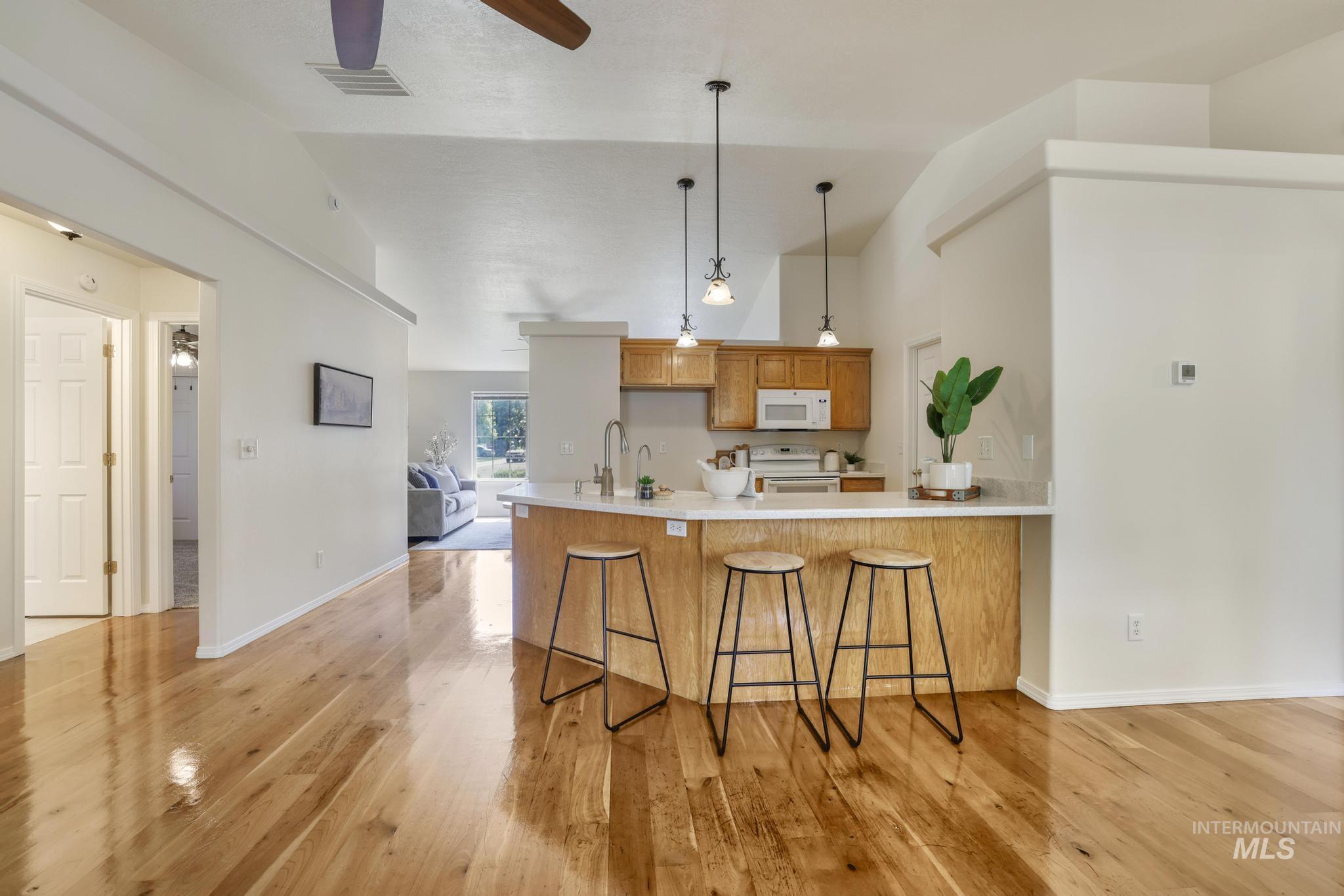 Kitchen featuring a breakfast bar, a peninsula, light wood-style flooring, pendant lighting, and white appliances