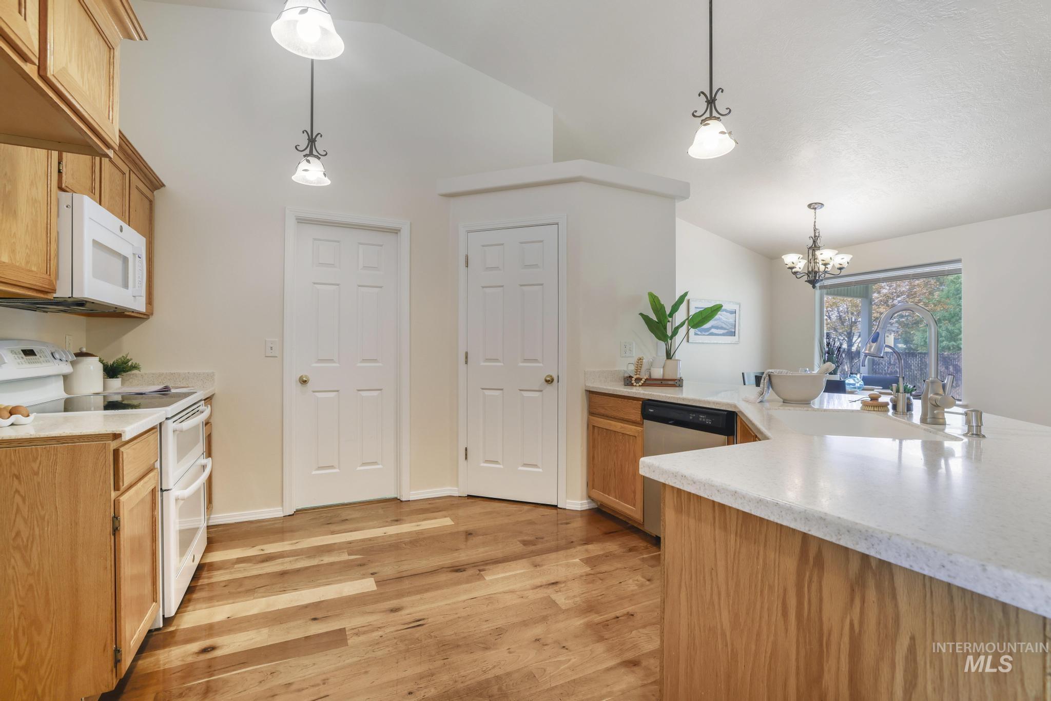 Kitchen featuring lofted ceiling, white appliances, pendant lighting, light wood-style flooring, and a chandelier