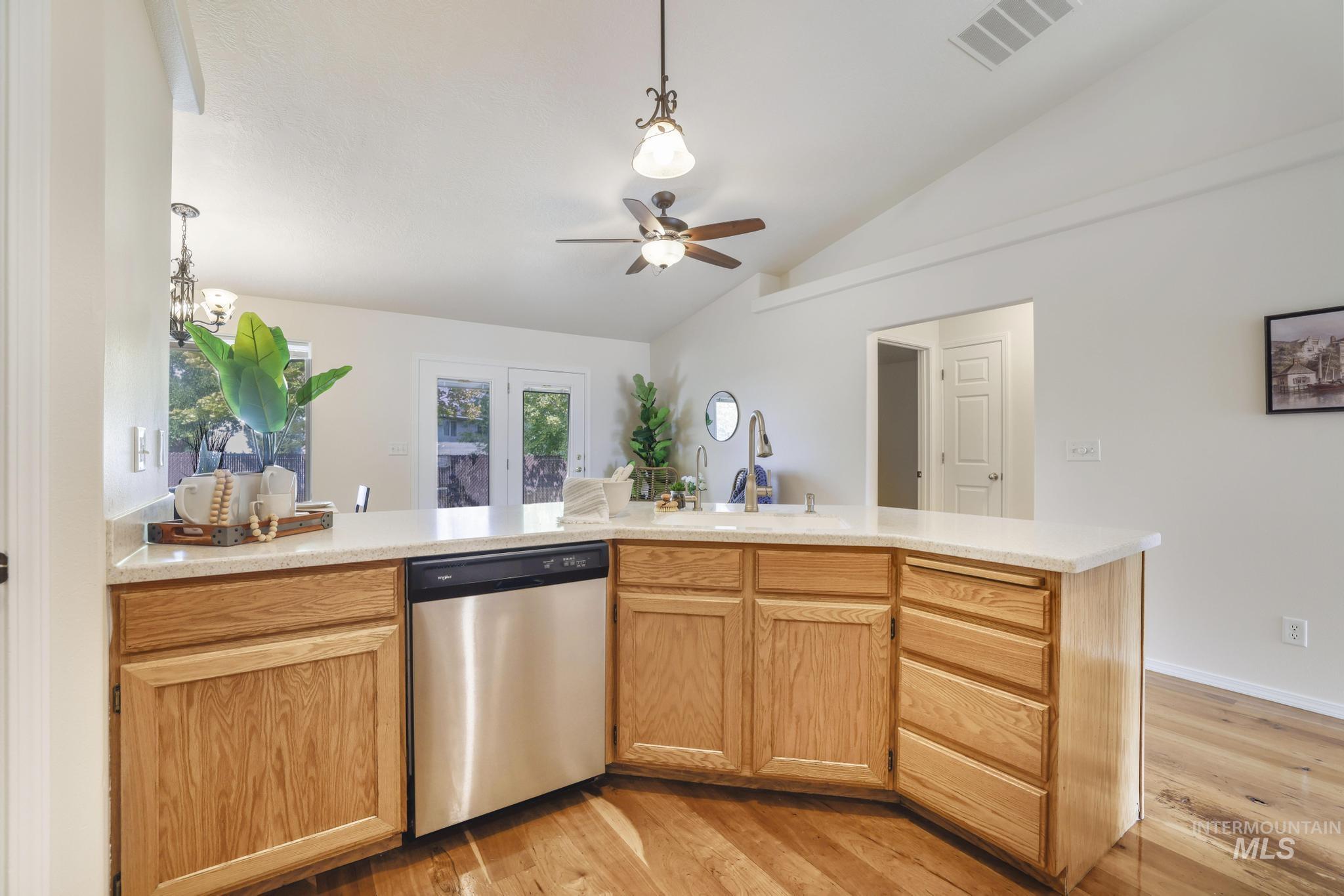 Kitchen featuring stainless steel dishwasher, pendant lighting, light wood-style flooring, vaulted ceiling, and a peninsula