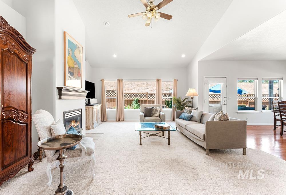 Living room with plenty of natural light, lofted ceiling, a ceiling fan, a glass covered fireplace, and light carpet