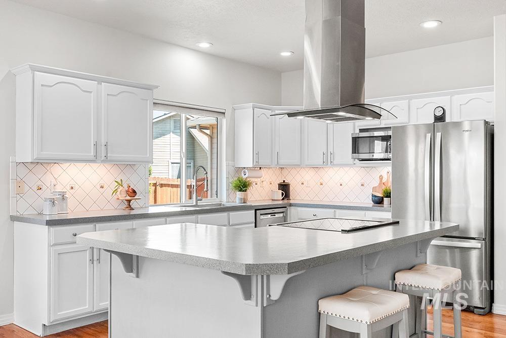 Kitchen featuring island exhaust hood, stainless steel appliances, a breakfast bar area, white cabinetry, and recessed lighting