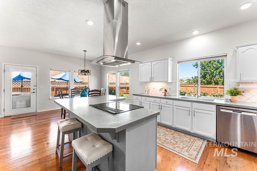 Kitchen featuring dishwasher, island range hood, black electric cooktop, white cabinets, and a textured ceiling