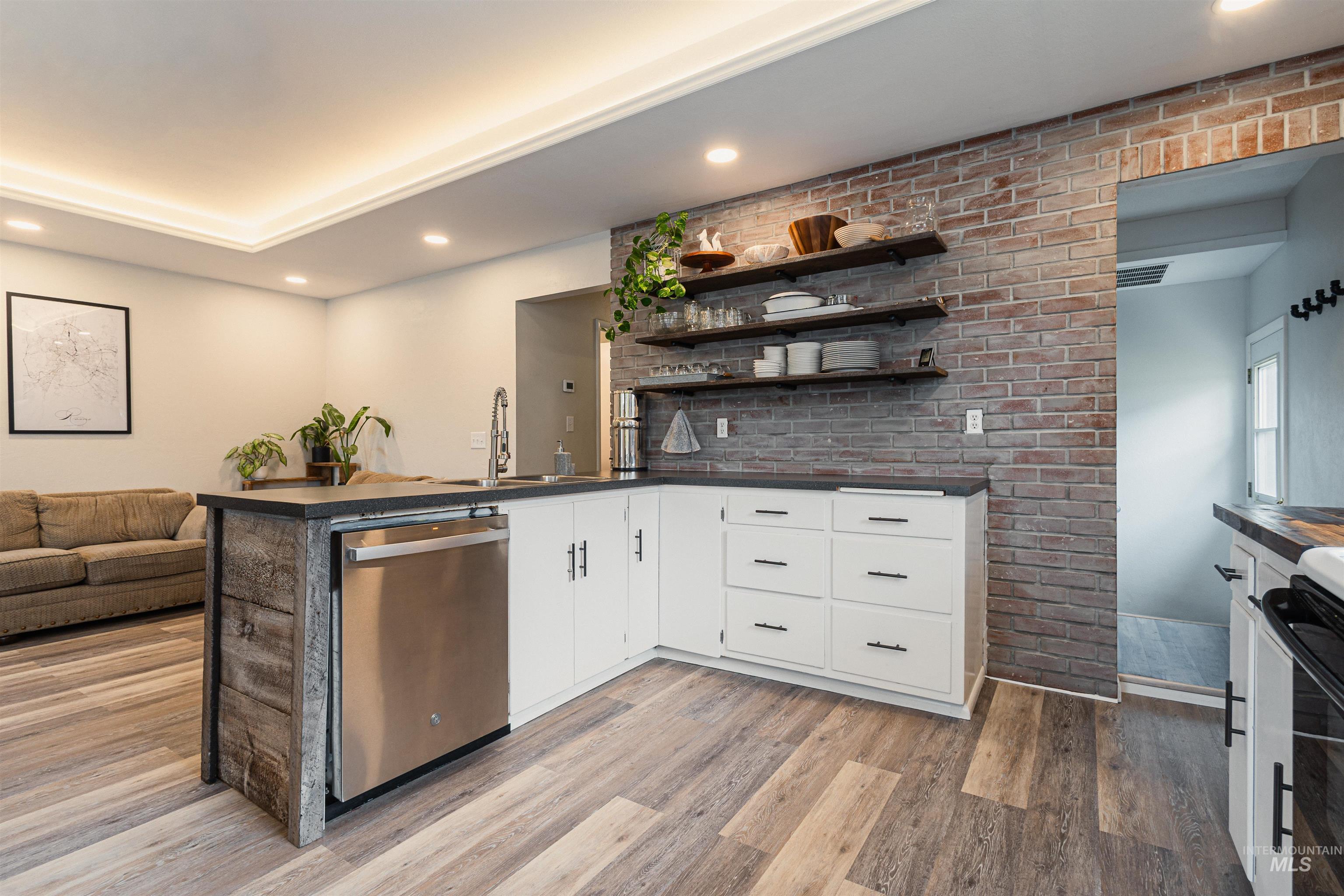 Kitchen with dark countertops, open shelves, black / electric stove, brick wall, and freestanding refrigerator