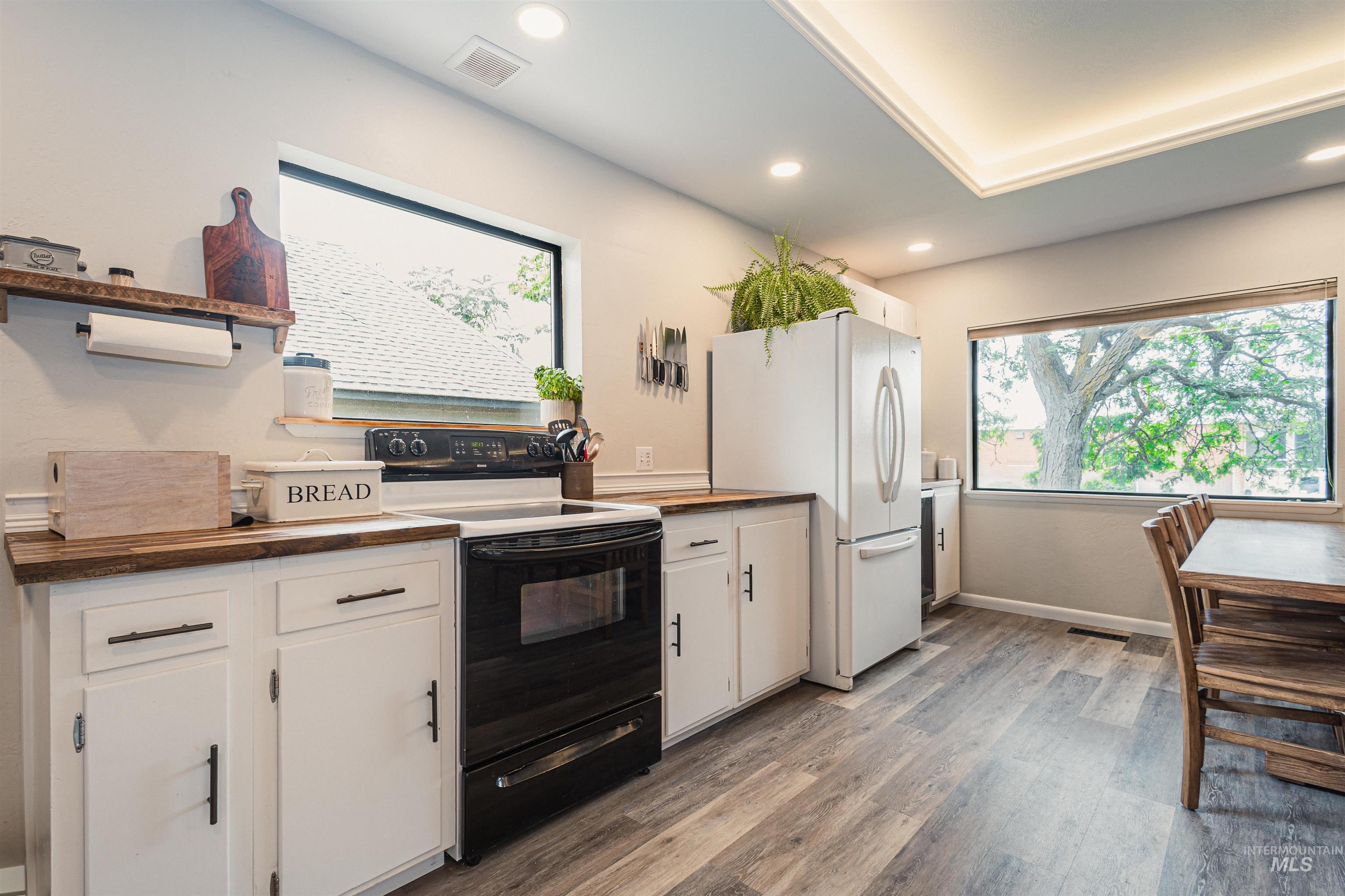 Living area featuring a tray ceiling, ceiling fan, light wood finished floors, recessed lighting, and bar with sink