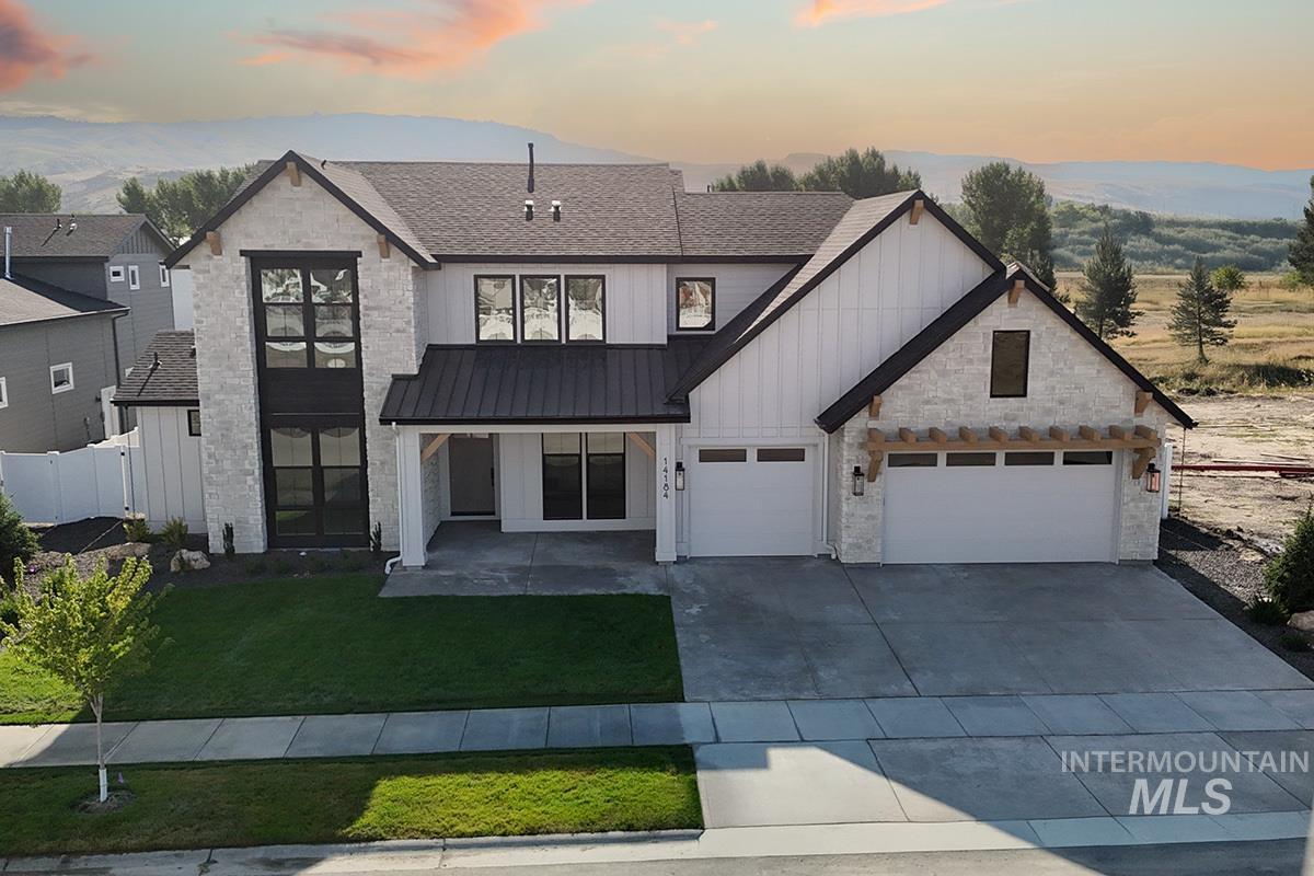 Modern farmhouse featuring board and batten siding, driveway, a yard, stone siding, and a garage