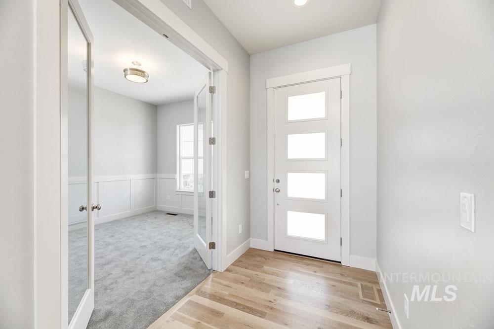 Foyer entrance featuring light wood-type flooring, light colored carpet, french doors, and a wainscoted wall