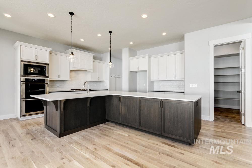 Kitchen with white cabinets, decorative backsplash, a large island with sink, recessed lighting, and decorative light fixtures