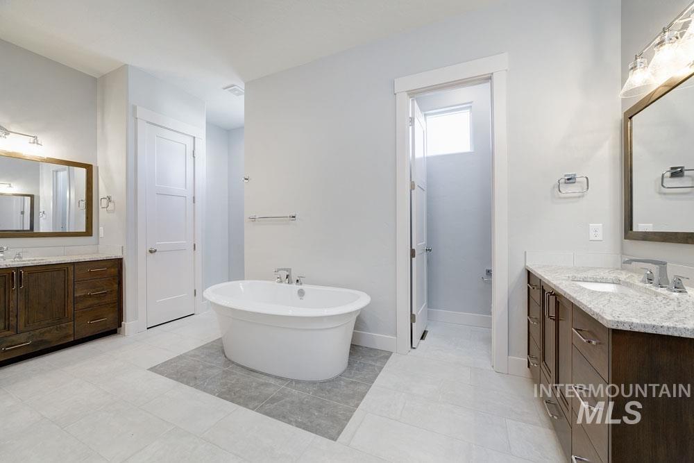 Bathroom featuring a soaking tub, two vanities, and light tile patterned floors