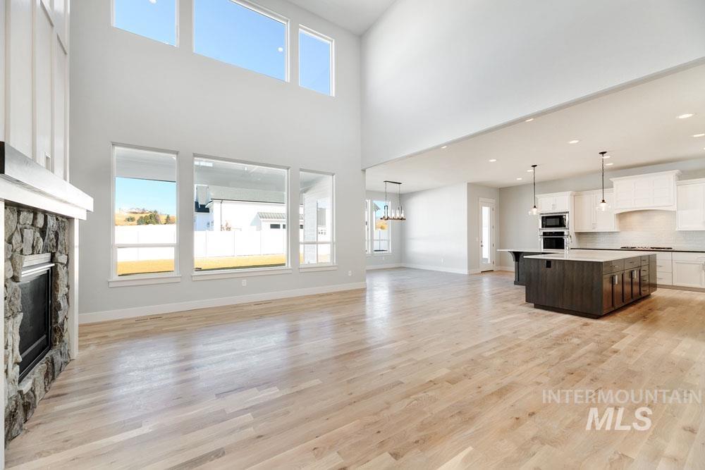 Unfurnished living room with healthy amount of natural light, light wood-style flooring, a fireplace, a towering ceiling, and recessed lighting