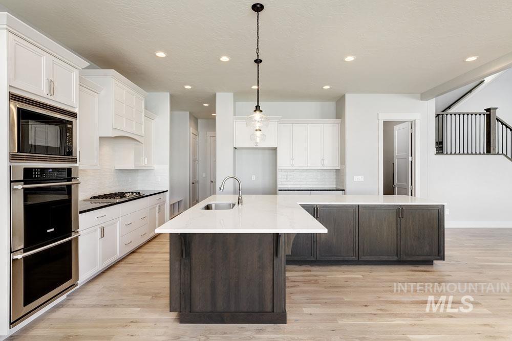 Kitchen with a spacious island, appliances with stainless steel finishes, white cabinetry, dark brown cabinets, and recessed lighting