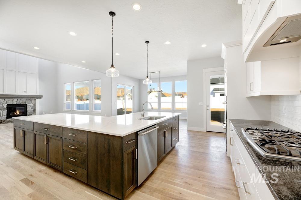 Kitchen with white cabinets, a fireplace, hanging light fixtures, open floor plan, and light wood finished floors