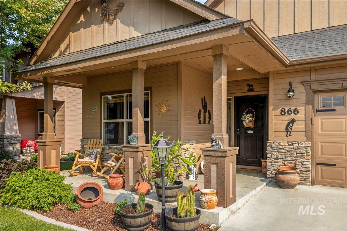 View of exterior entry featuring board and batten siding, covered porch, stone siding, and a shingled roof