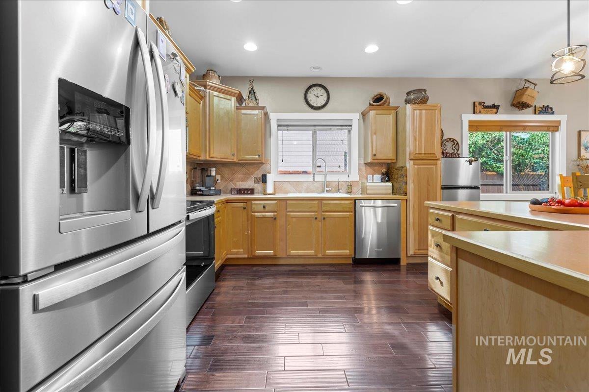 Kitchen featuring stainless steel appliances, decorative backsplash, light countertops, light brown cabinets, and dark wood-type flooring