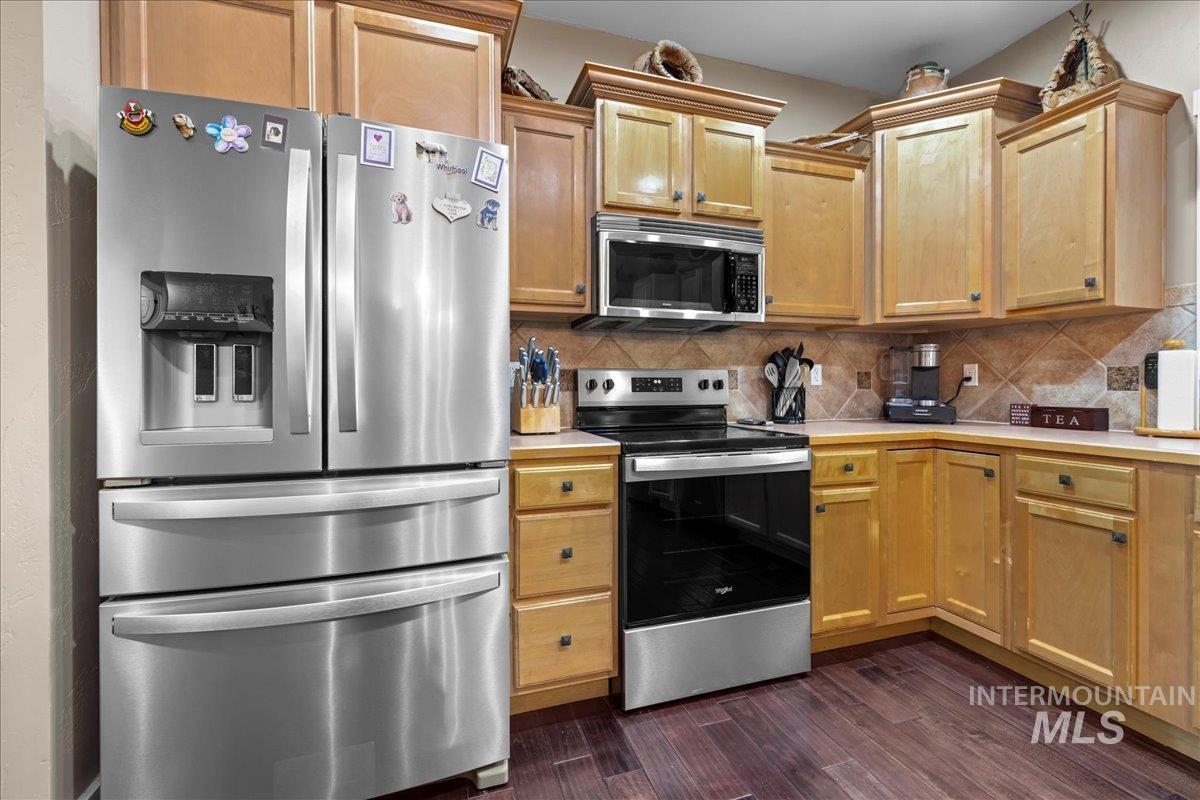 Kitchen featuring appliances with stainless steel finishes, light countertops, decorative backsplash, and dark wood finished floors