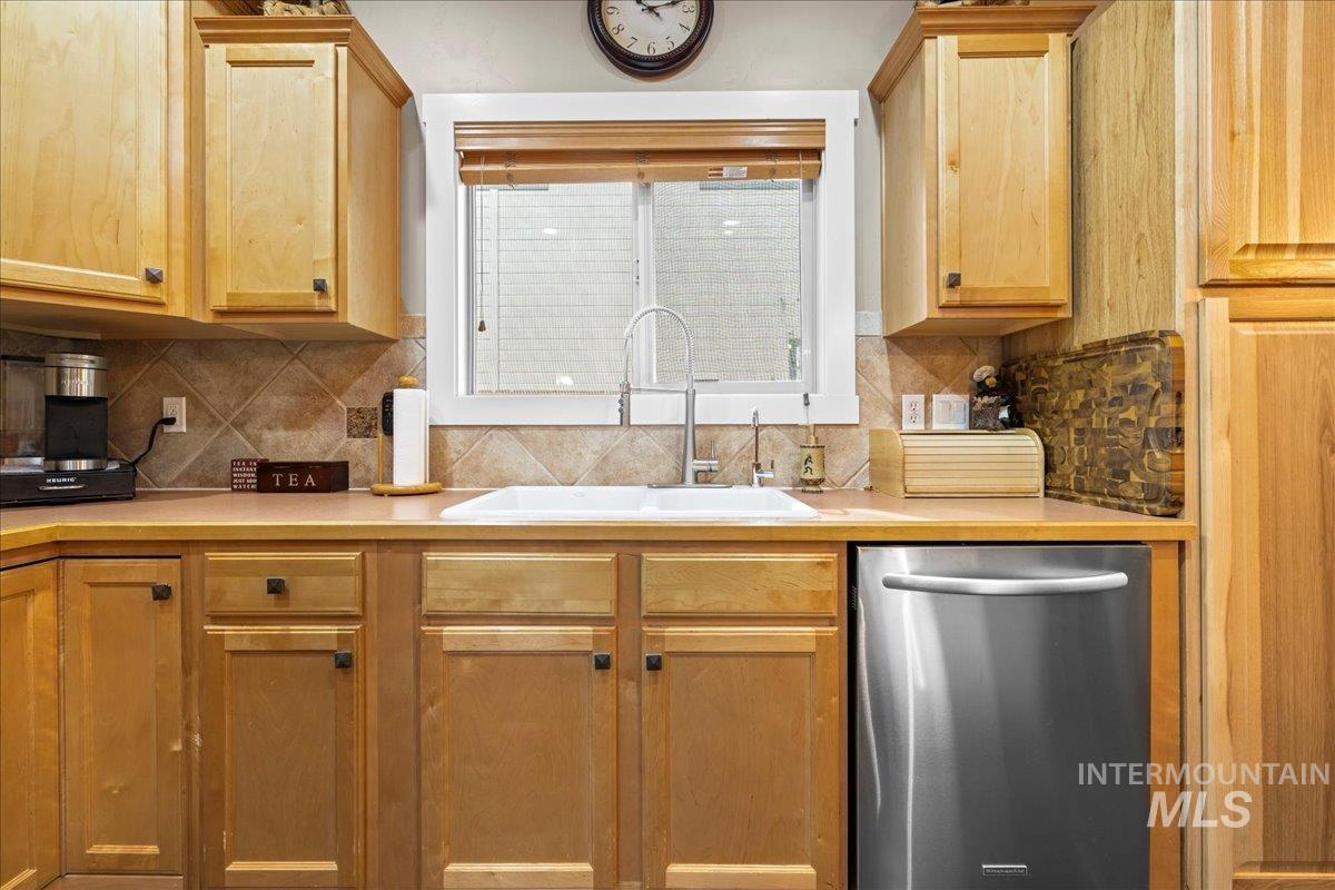Kitchen featuring light countertops, stainless steel dishwasher, and backsplash
