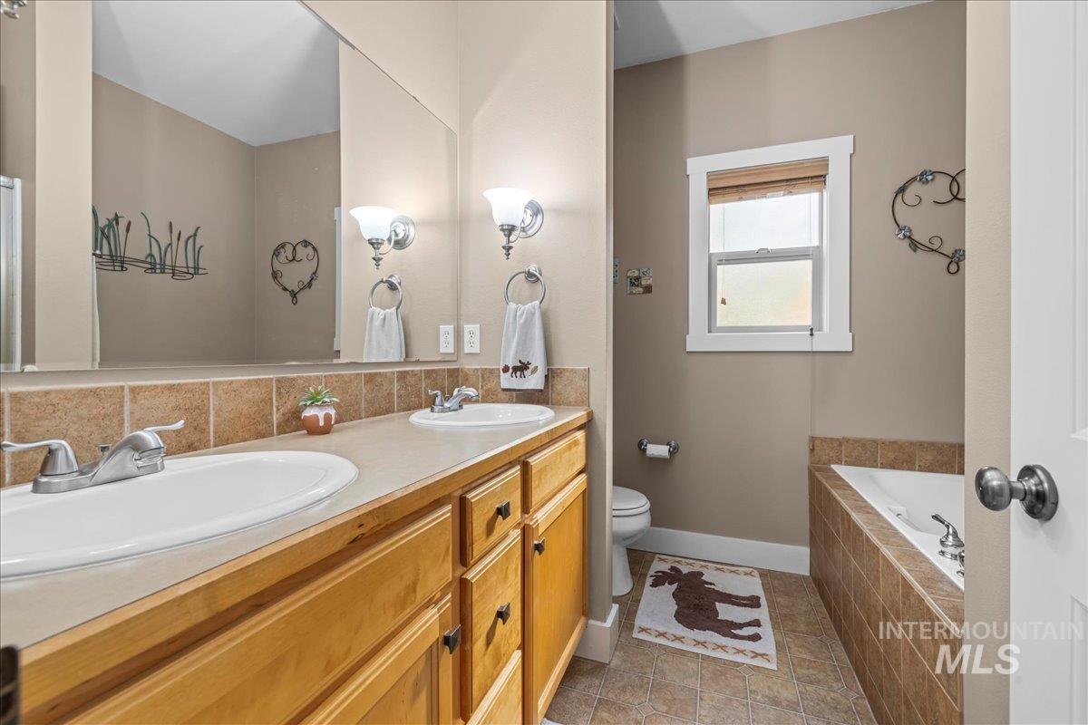 Full bath with a garden tub, double vanity, light tile patterned floors, and backsplash