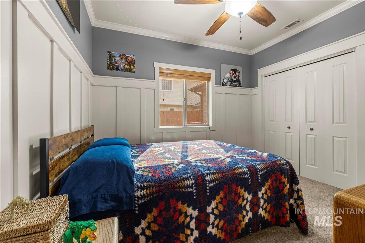 Carpeted bedroom with crown molding, a decorative wall, a closet, a wainscoted wall, and ceiling fan