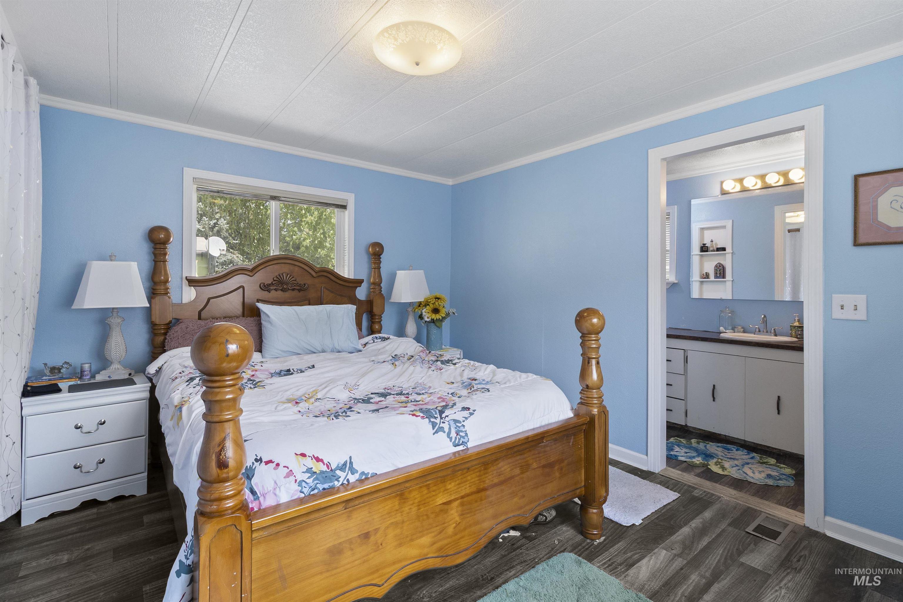 Bedroom with crown molding, dark wood finished floors, and connected bathroom