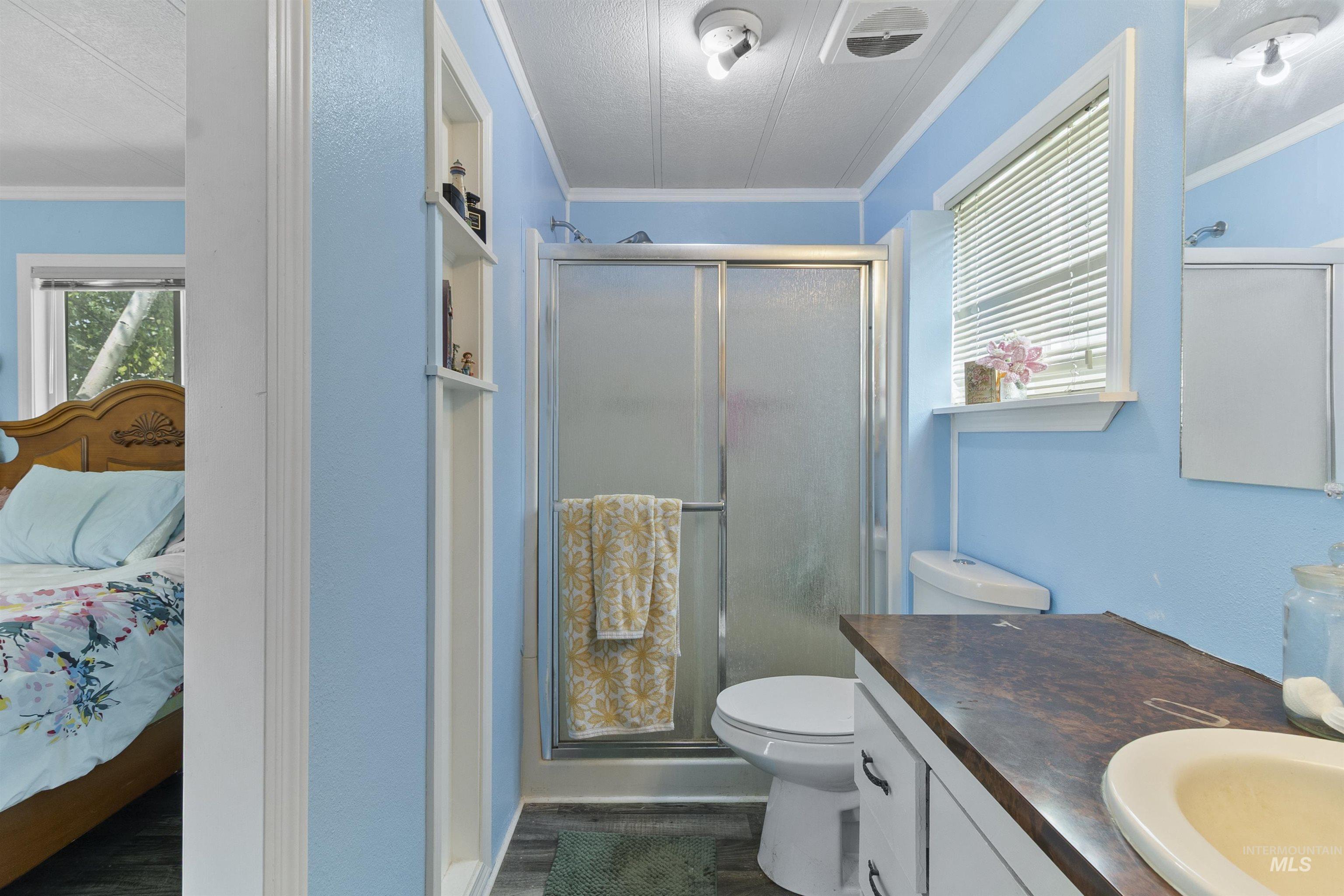 Ensuite bathroom featuring crown molding, a shower stall, vanity, dark wood finished floors, and a textured ceiling