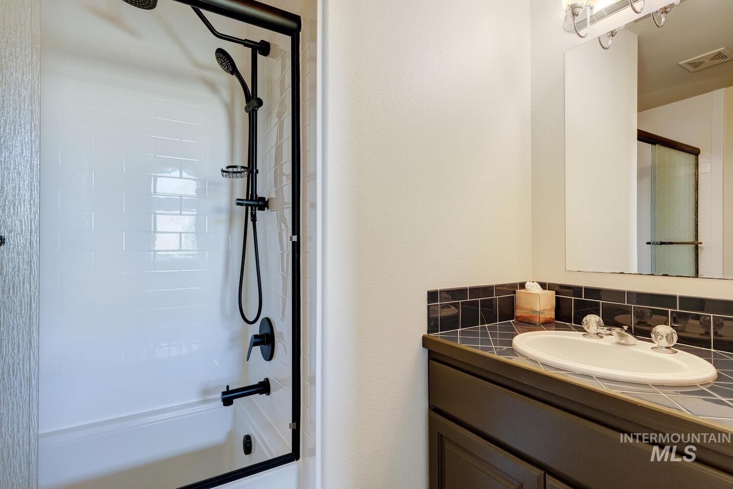 Bathroom featuring vanity, combined bath / shower with glass door, and decorative backsplash