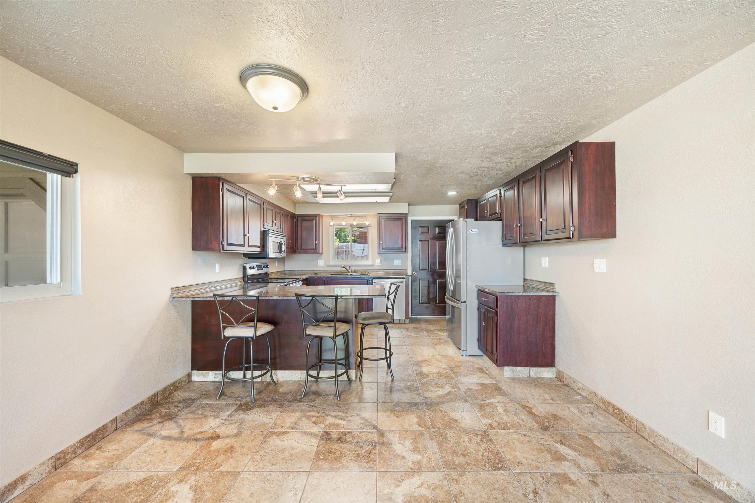 Kitchen featuring a textured ceiling, a breakfast bar, a peninsula, and appliances with stainless steel finishes