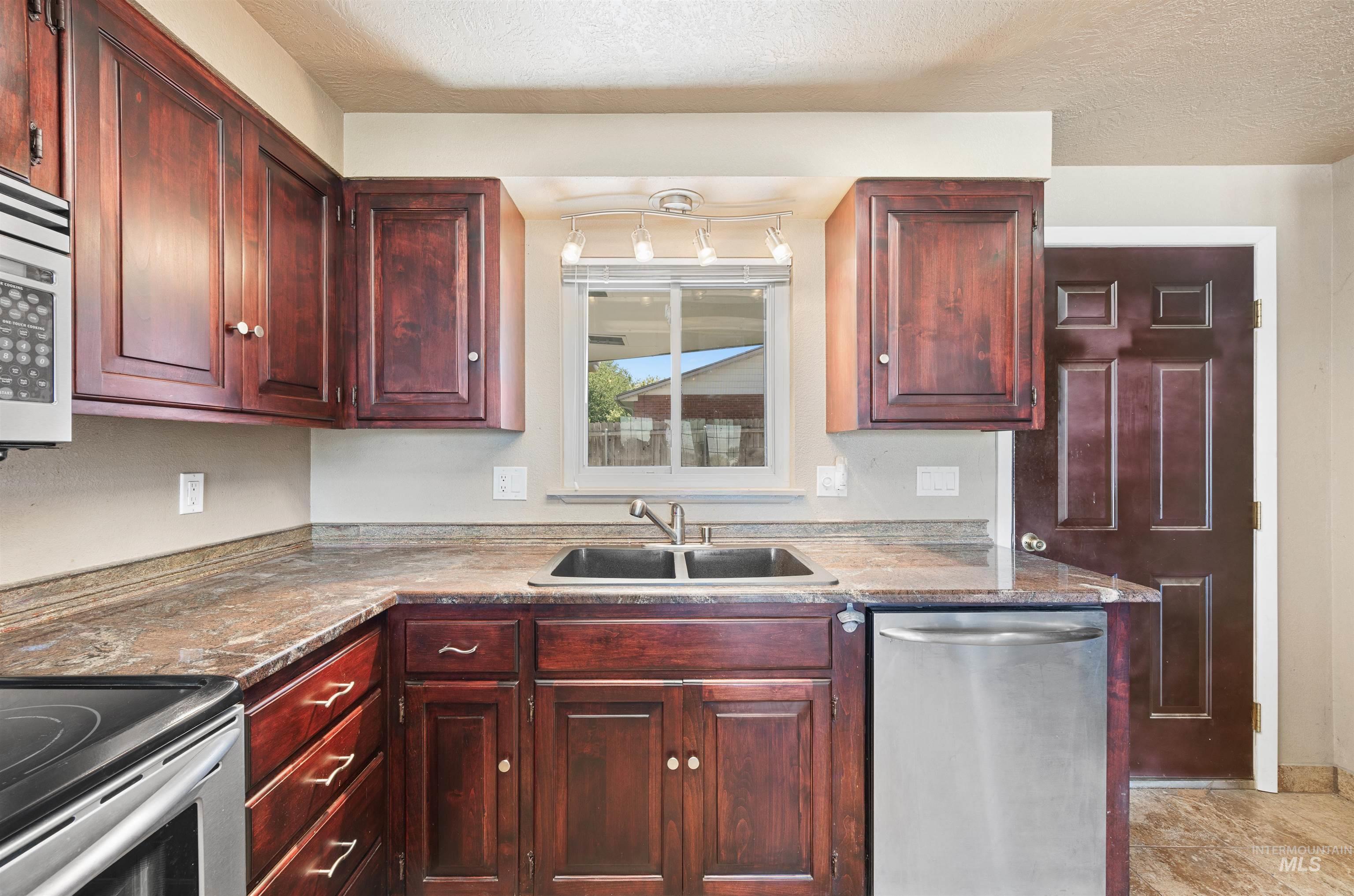 Kitchen featuring appliances with stainless steel finishes, reddish brown cabinets, a textured ceiling, and light stone countertops