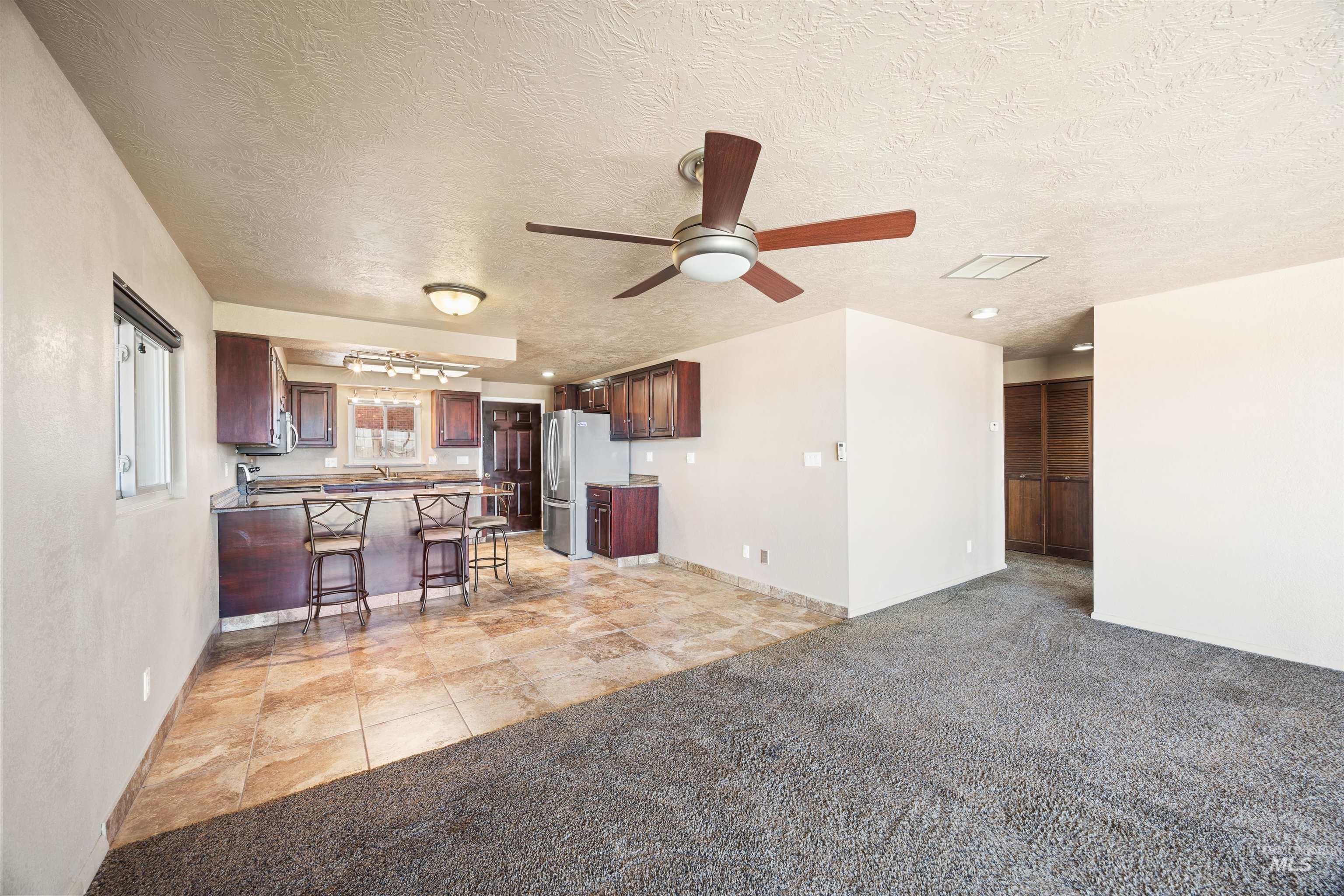 Kitchen with light carpet, a ceiling fan, open floor plan, a kitchen breakfast bar, and a textured ceiling