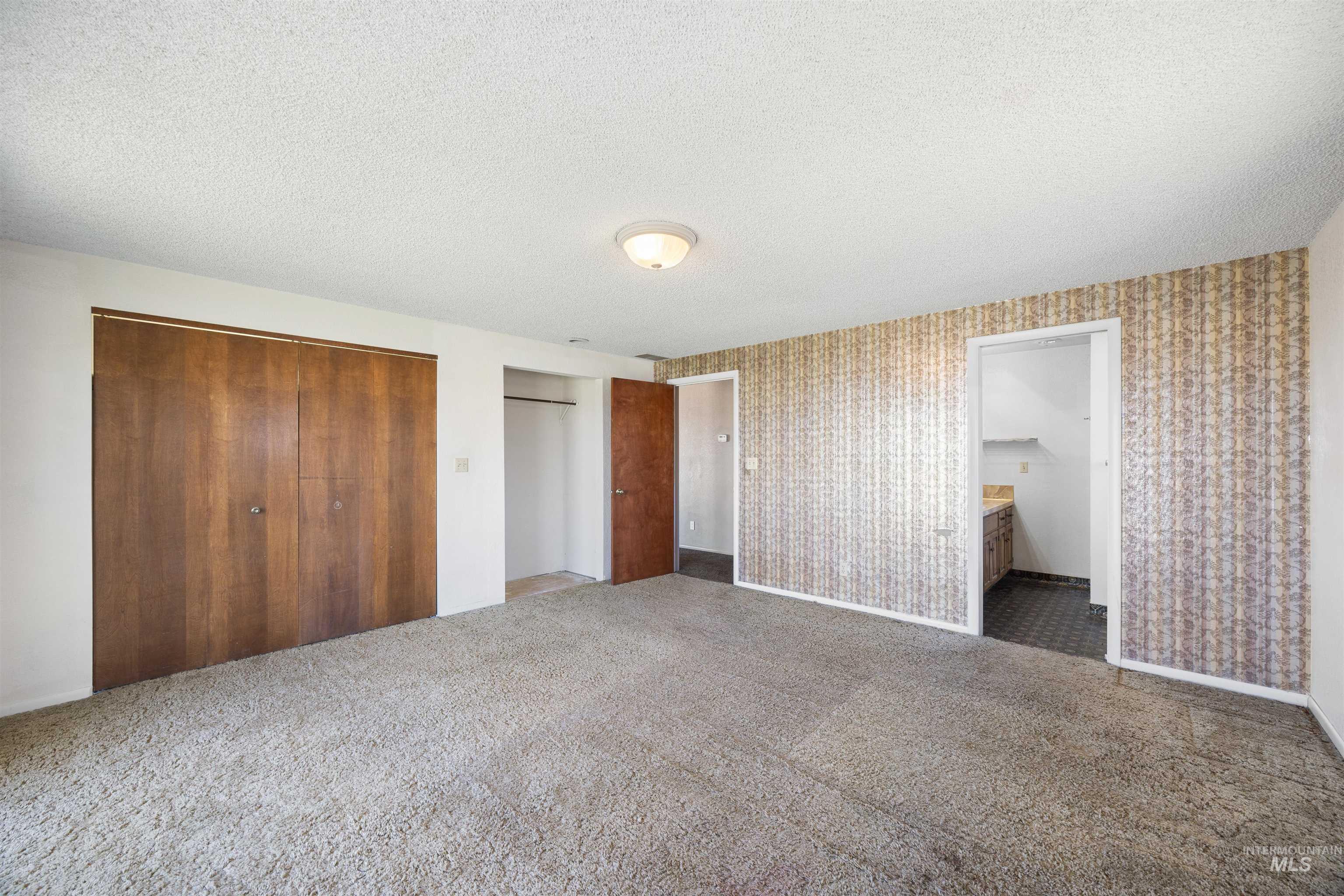 Unfurnished bedroom featuring carpet floors, a closet, a textured ceiling, and ensuite bath