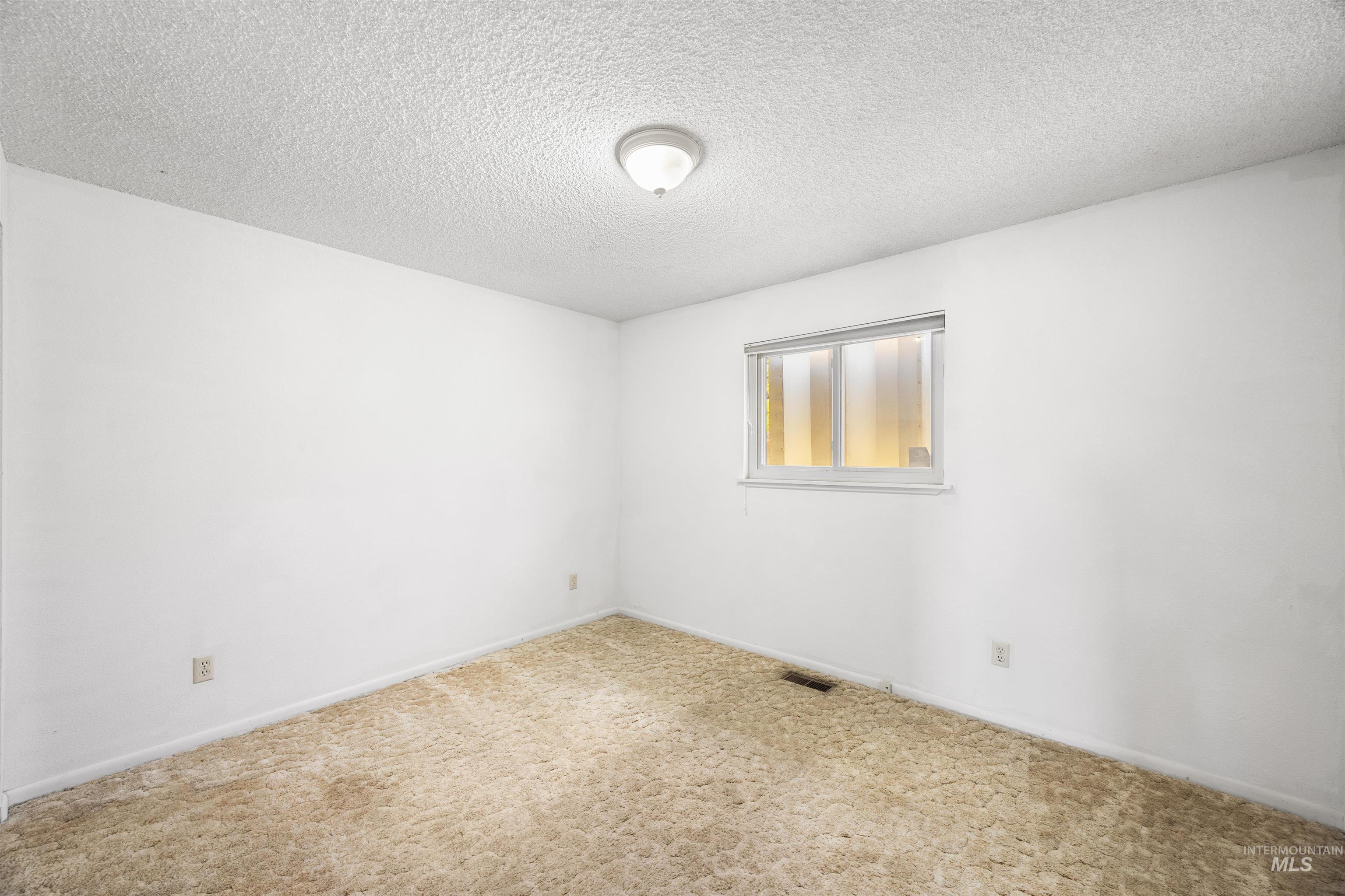 Carpeted empty room featuring a textured ceiling and baseboards