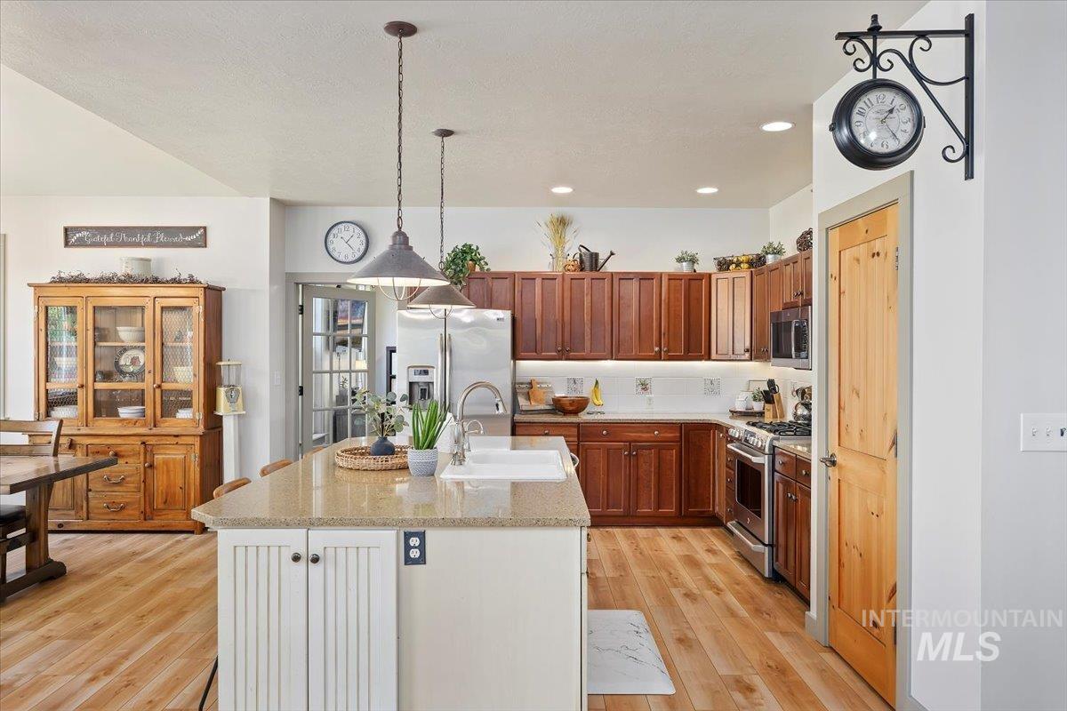 Kitchen with light stone countertops, pendant lighting, appliances with stainless steel finishes, brown cabinets, and light wood-style flooring