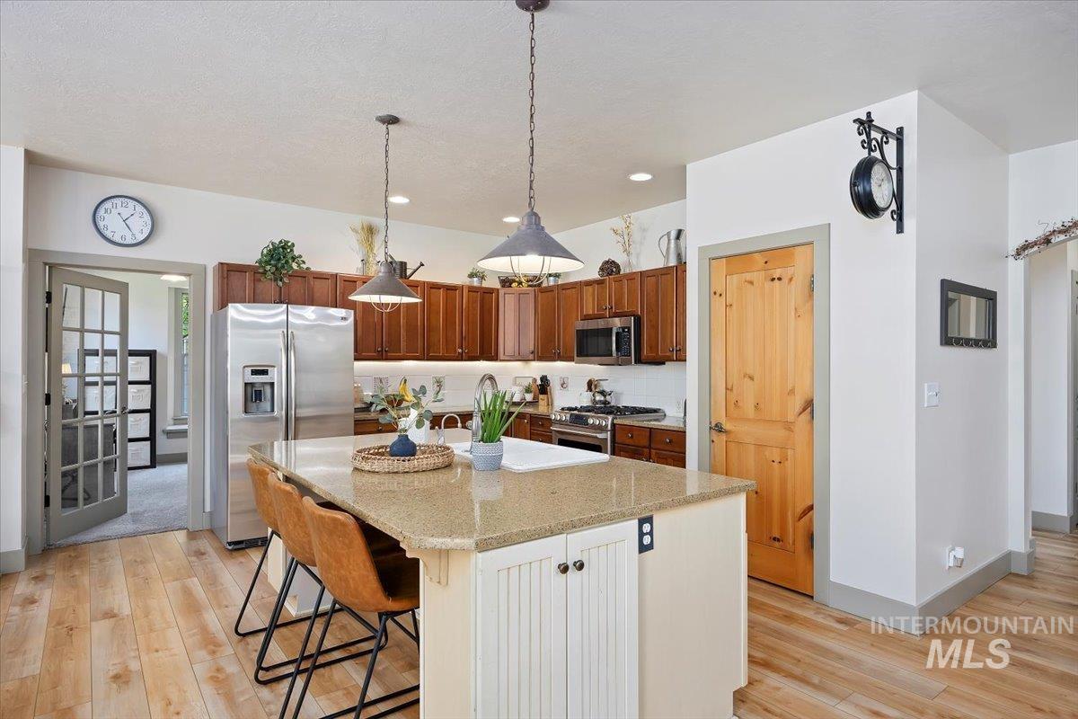 Kitchen featuring appliances with stainless steel finishes, a kitchen bar, light stone counters, decorative light fixtures, and light wood-style floors