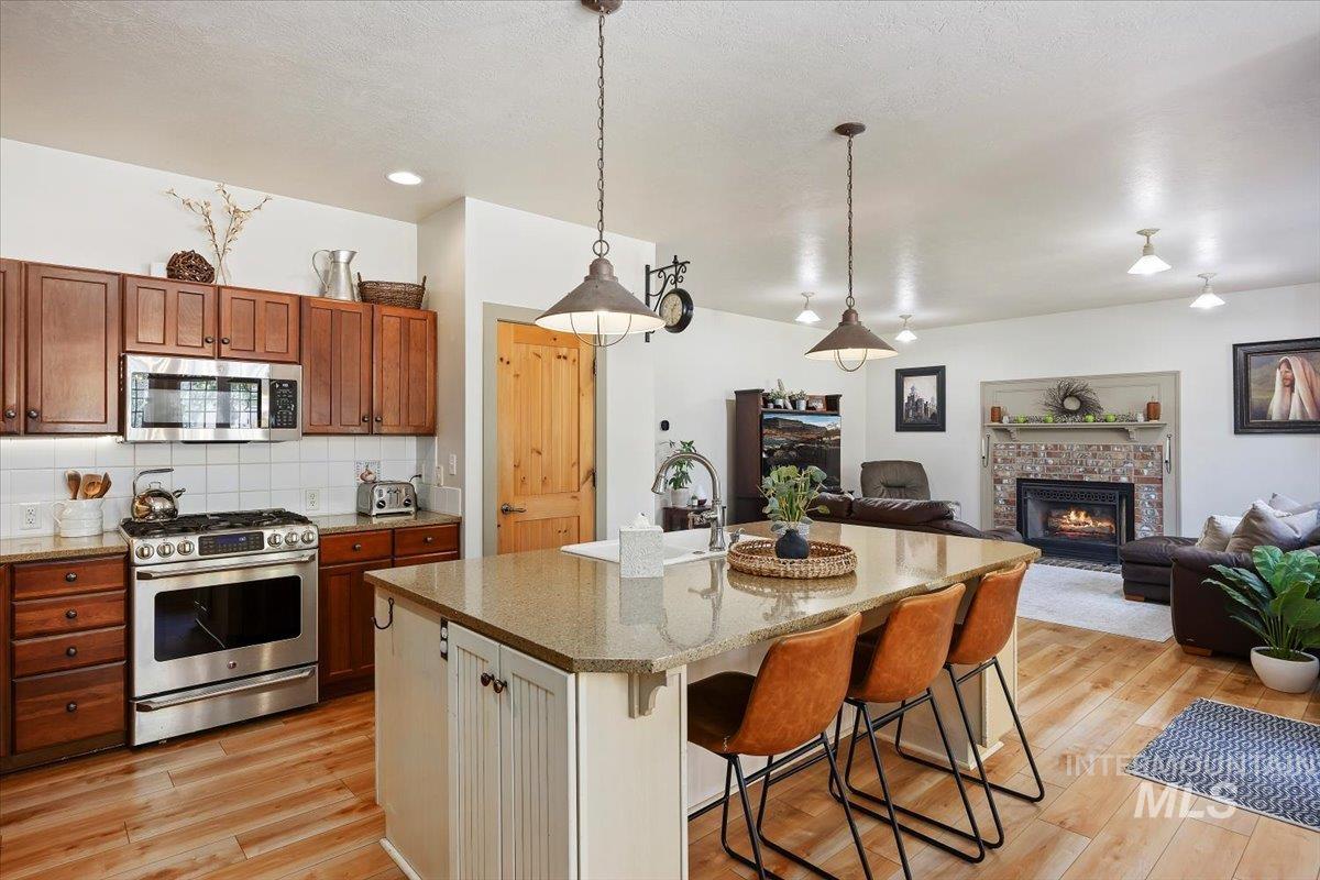 Kitchen with a kitchen bar, appliances with stainless steel finishes, open floor plan, hanging light fixtures, and light stone countertops