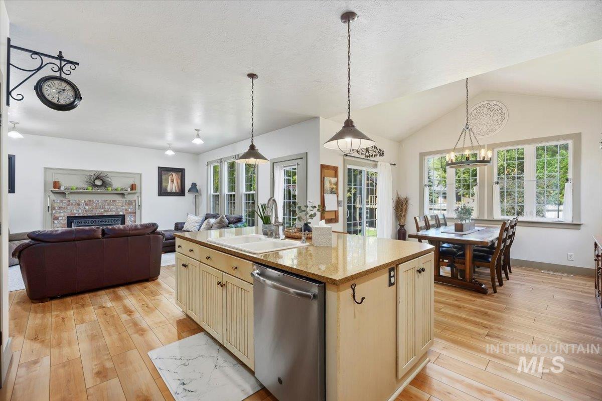 Kitchen featuring stainless steel dishwasher, pendant lighting, light stone countertops, plenty of natural light, and lofted ceiling