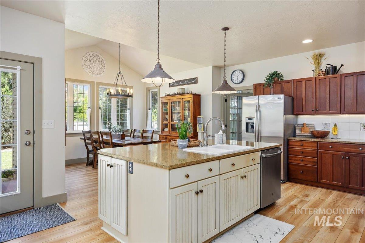 Kitchen featuring decorative light fixtures, light stone countertops, backsplash, stainless steel dishwasher, and plenty of natural light