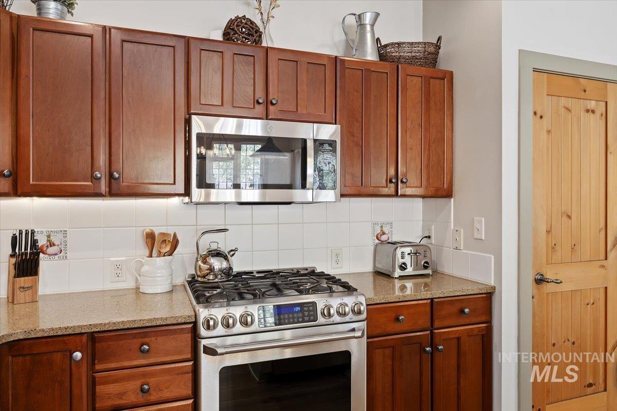 Kitchen featuring stainless steel appliances, brown cabinets, decorative backsplash, and light stone counters
