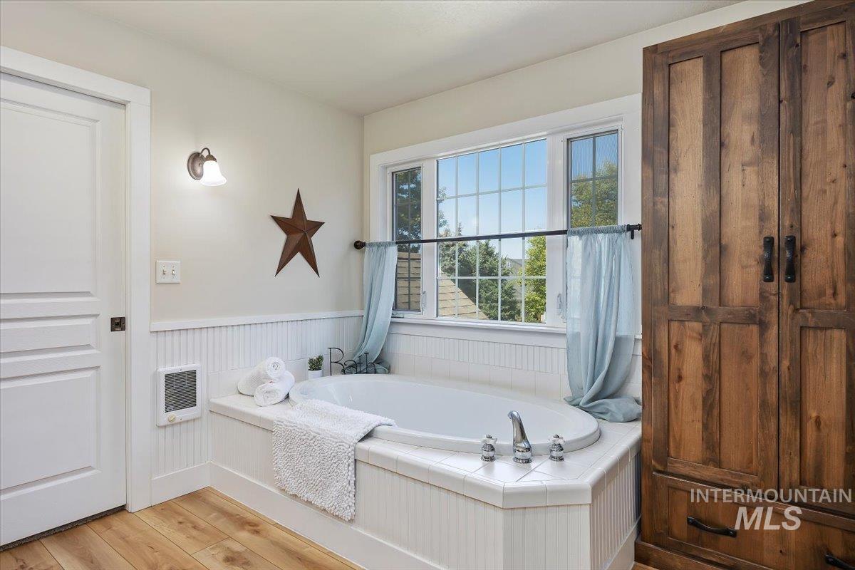 Full bathroom featuring light wood finished floors, a bath, heating unit, and wainscoting