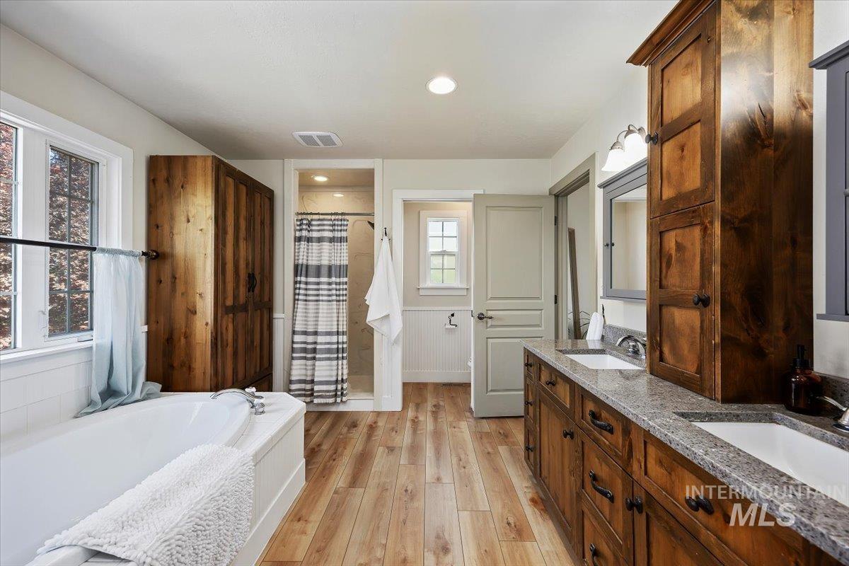Bathroom featuring double vanity, light wood-type flooring, a stall shower, a garden tub, and recessed lighting