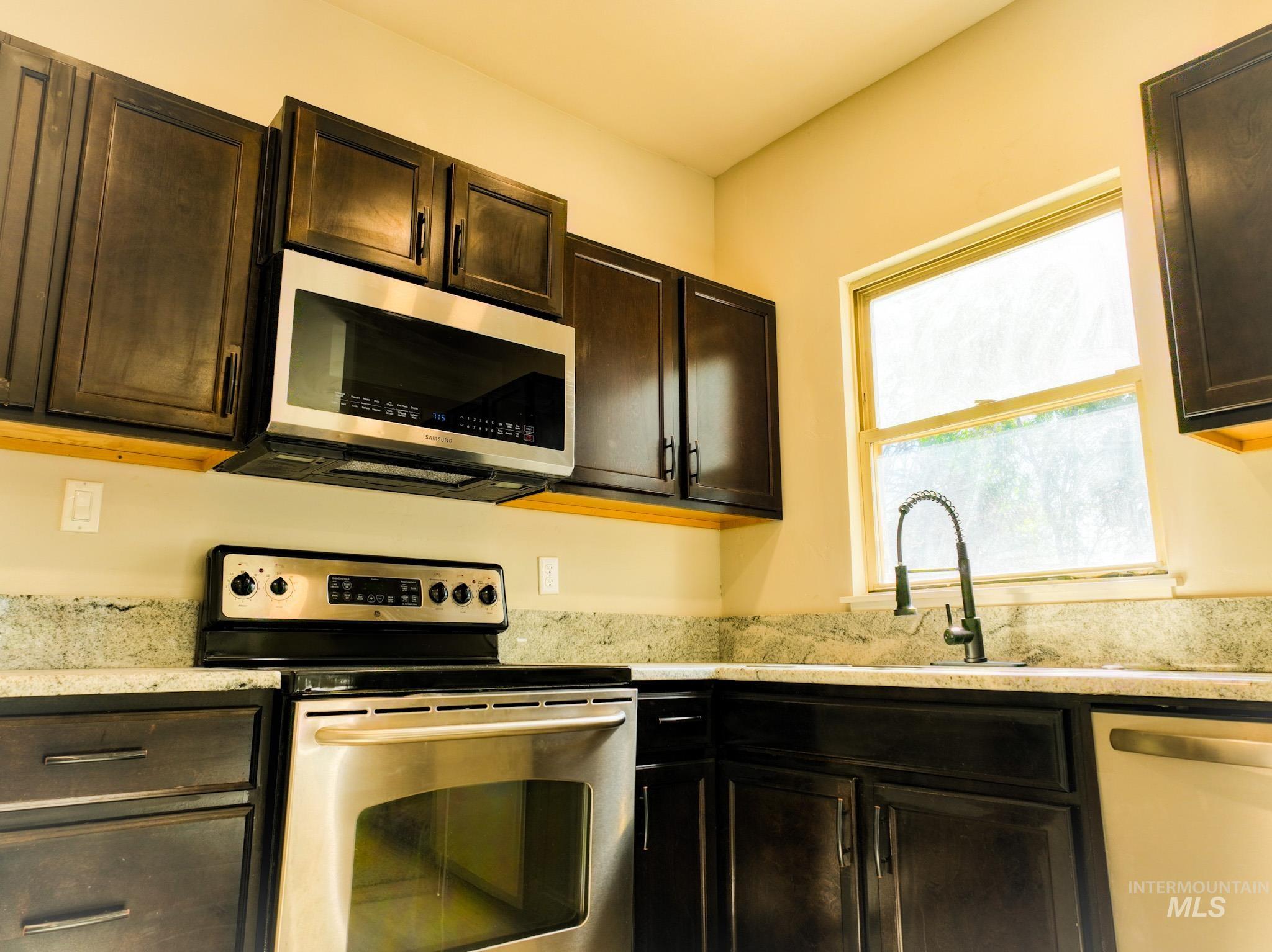 Kitchen featuring appliances with stainless steel finishes, dark brown cabinets, and light stone counters