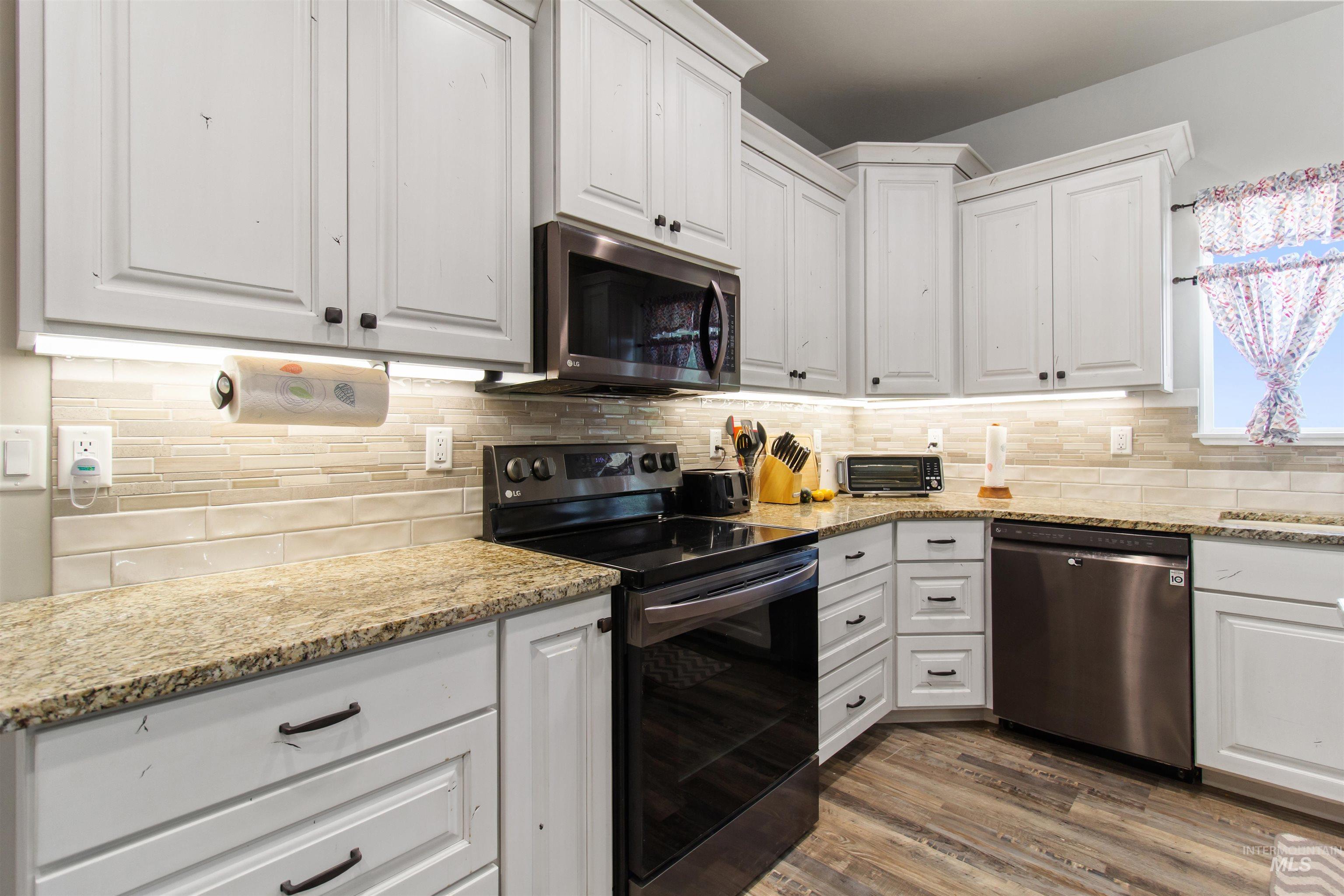Kitchen with stainless steel appliances, white cabinetry, and light stone counters