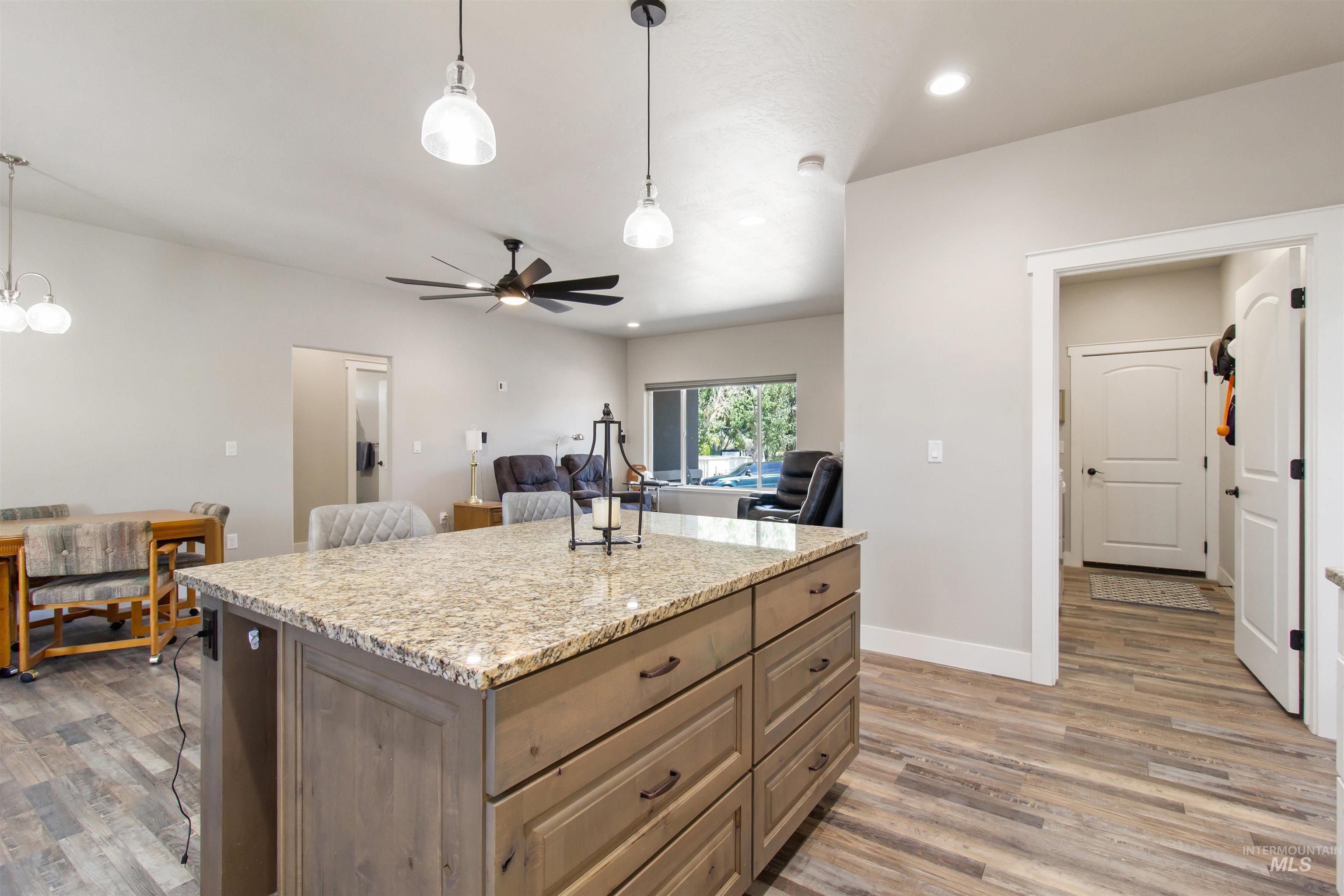 Kitchen with pendant lighting, light stone countertops, a ceiling fan, light wood finished floors, and a kitchen island
