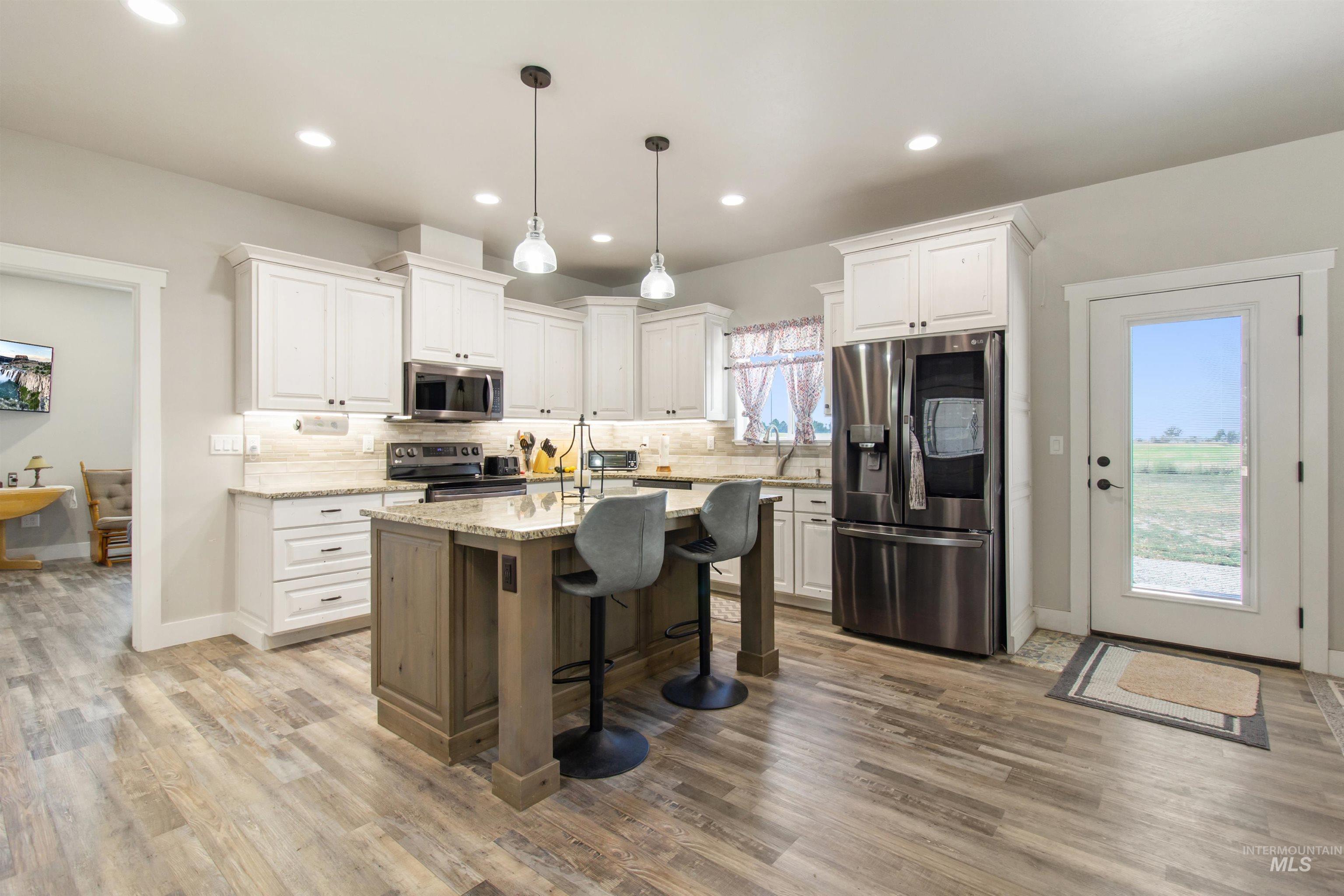 Kitchen with tasteful backsplash, stainless steel appliances, a breakfast bar area, light stone countertops, and white cabinetry