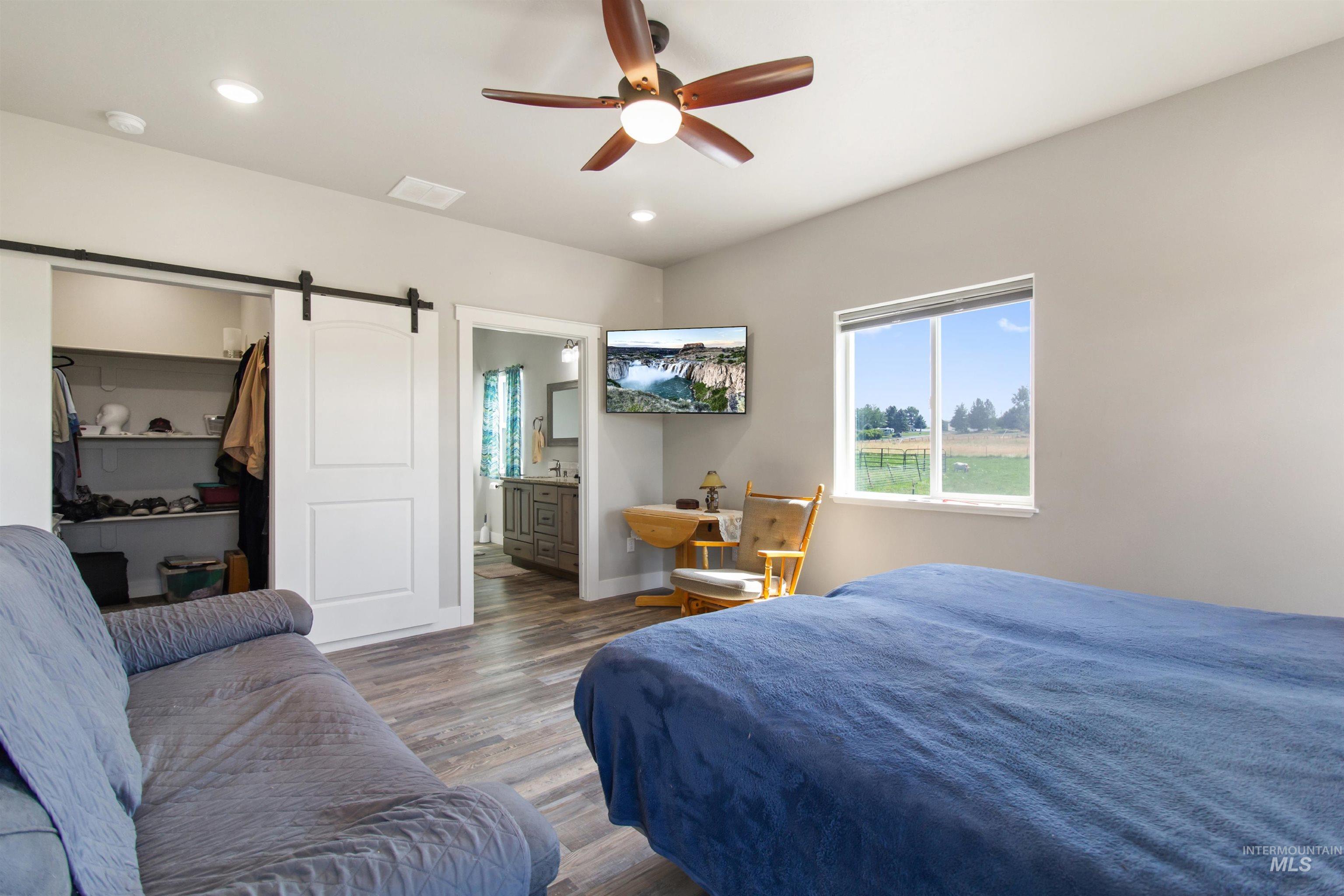 Bedroom featuring a barn door, wood finished floors, recessed lighting, a ceiling fan, and connected bathroom