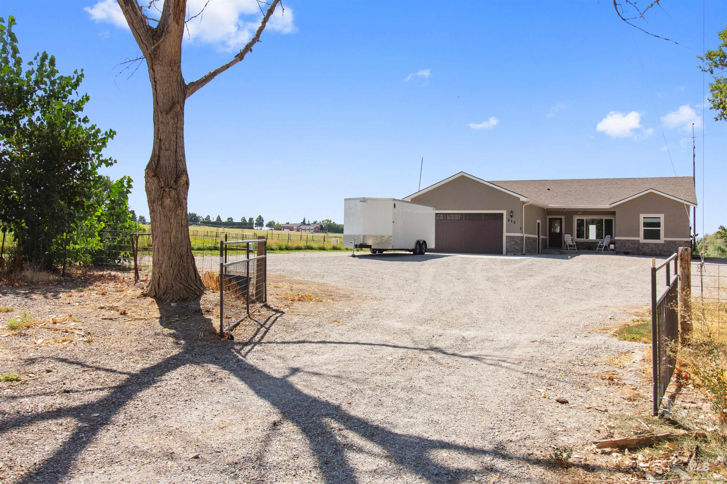 View of front of house with gravel driveway, stucco siding, an attached garage, a view of rural / pastoral area, and stone siding
