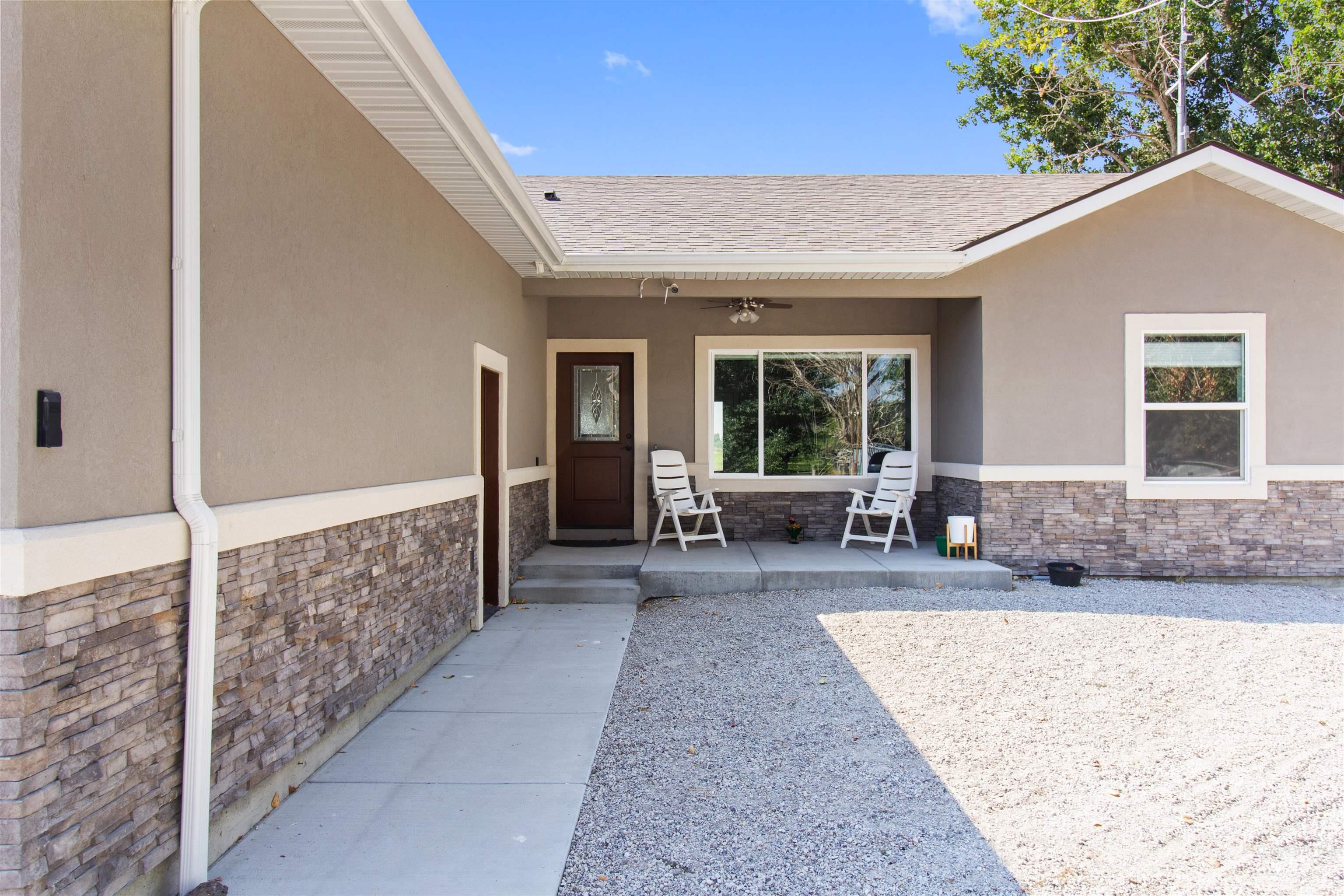 Doorway to property with stone siding, stucco siding, ceiling fan, and a porch