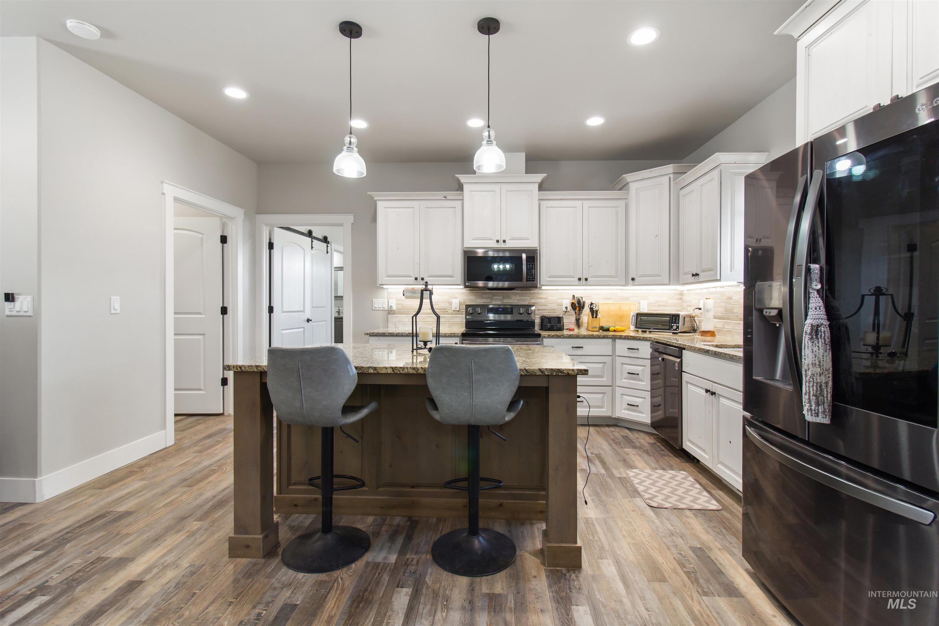 Kitchen with decorative backsplash, stainless steel appliances, light stone counters, white cabinets, and a center island with sink